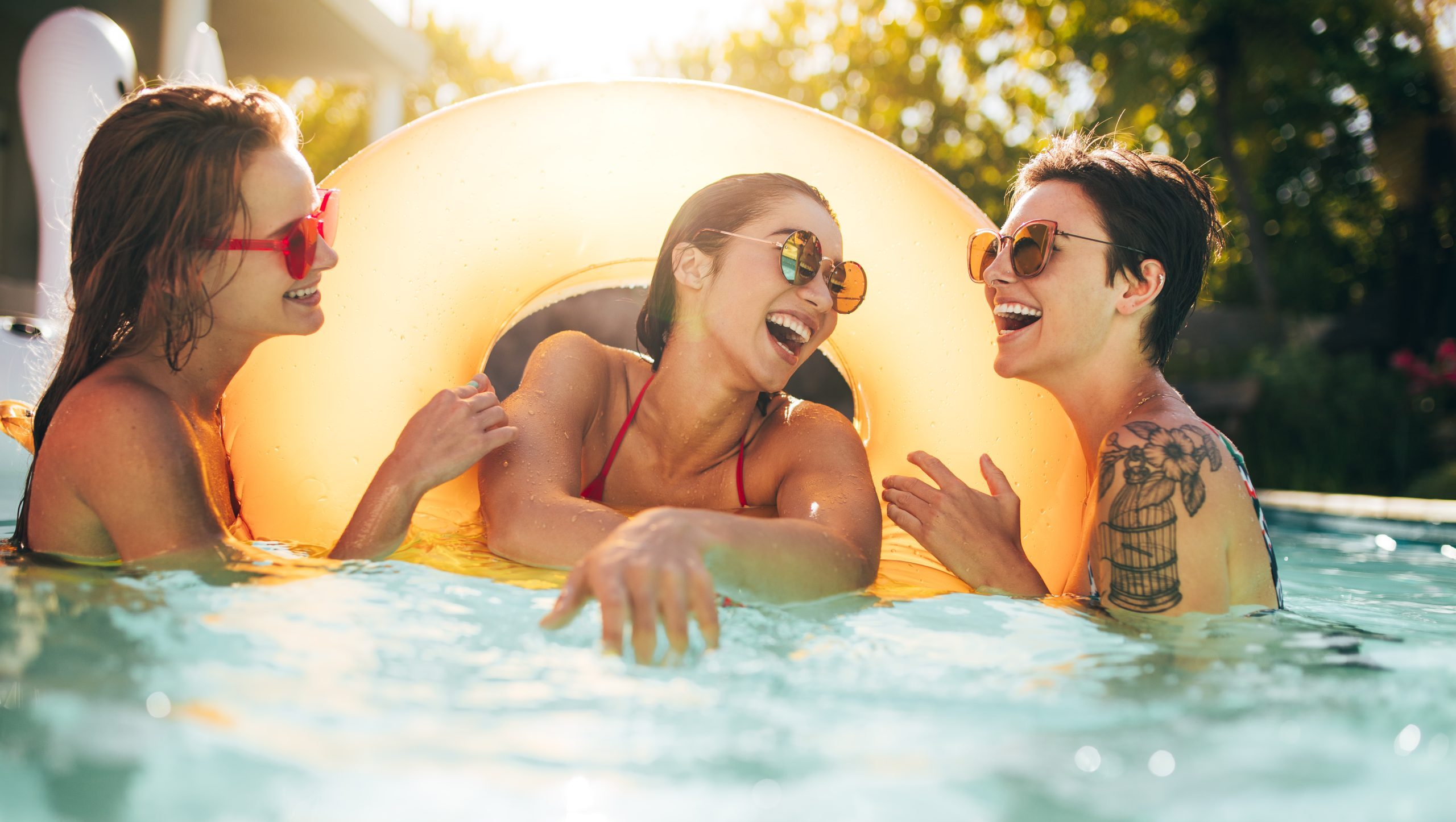 Three friends laughing together in above ground pool with yellow float