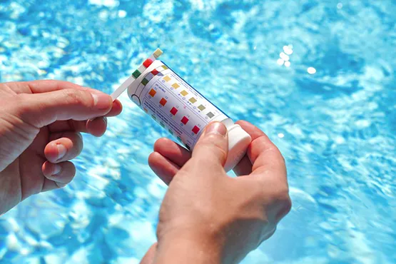 Person testing pool water chemistry with color-coded test strip kit