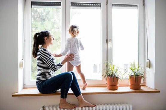 Woman and child sitting on window sill with potted plants indoors