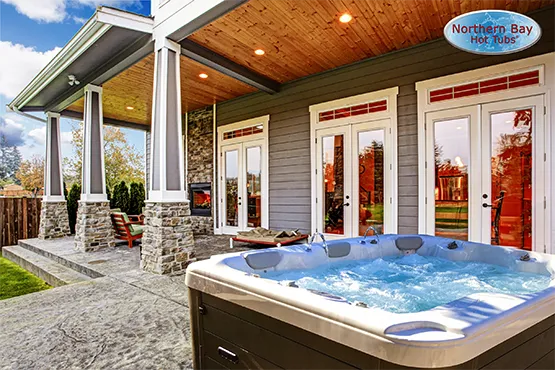 Luxury hot tub installed on backyard patio beside covered deck with glass doors